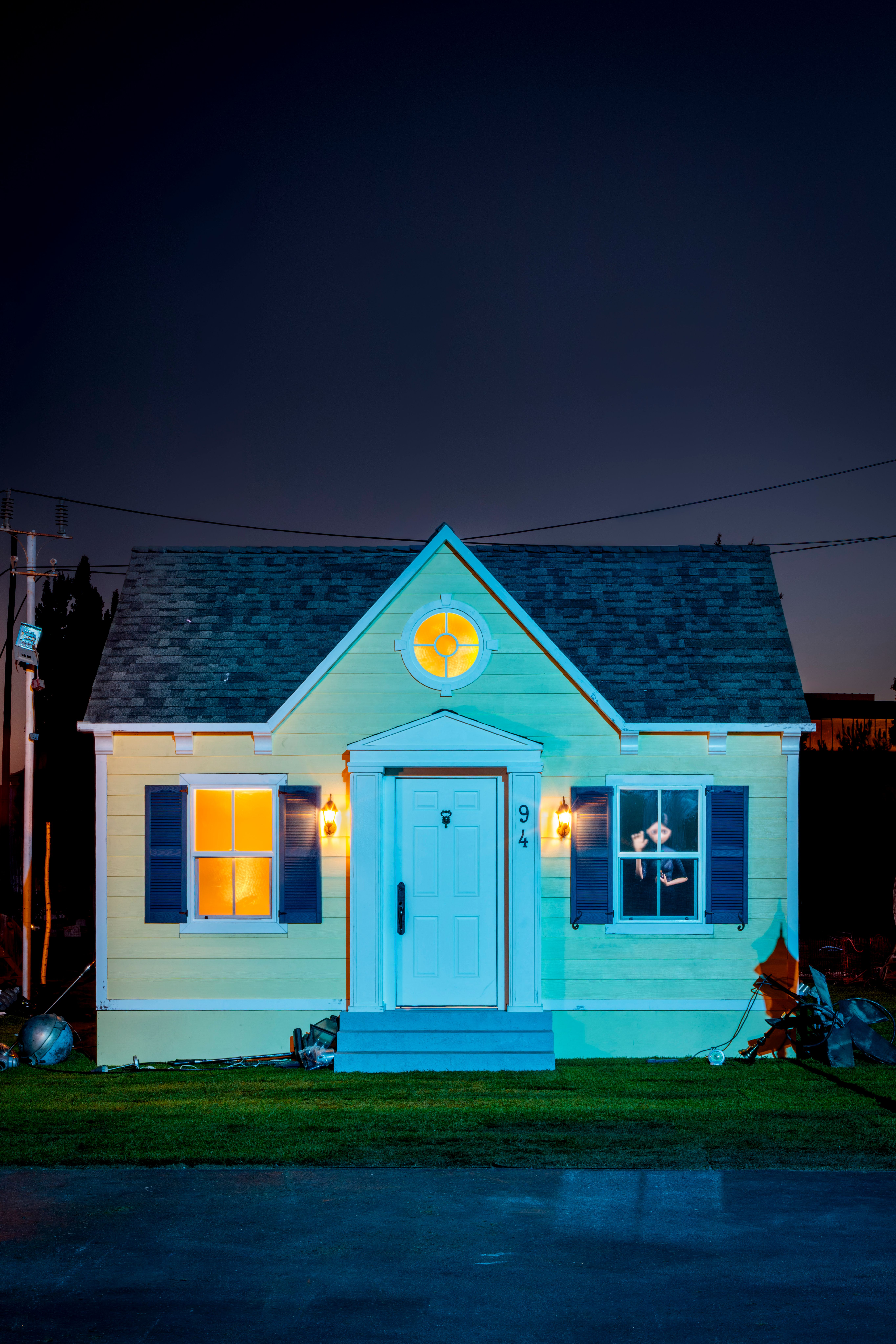 Small yellow house lit blue at night, with glowing windows and a person peering through one