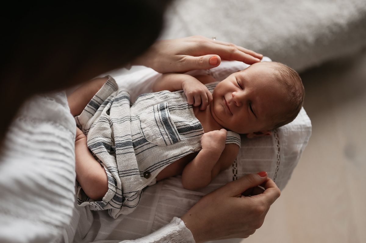 Liten nyfødt baby smiler i fanget til mamma