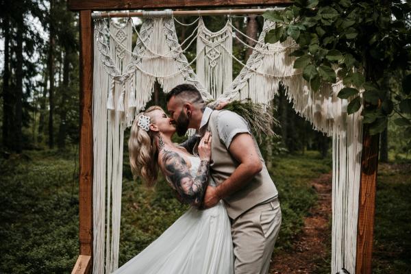 Brudepar som kysser under makrameportal i skogen