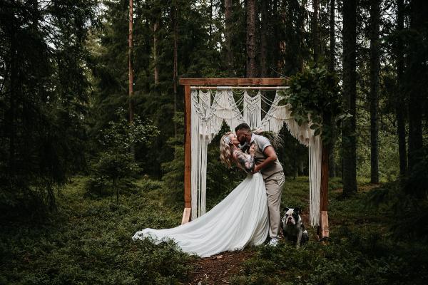 Brudepar kysser i skogen under en makrameportal