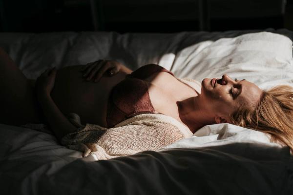 Gravid kvinne på senga i sollys