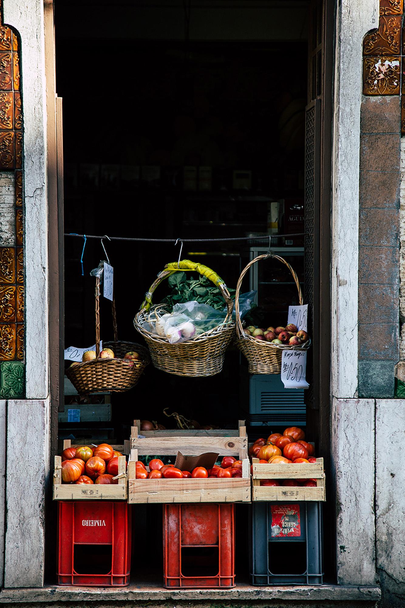 A street market scene with a variety of fresh produce, including fruits and vegetables, on display in baskets and crates.