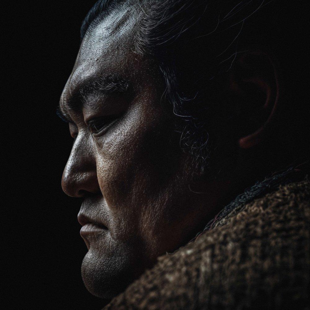 A close-up of a man's face with a rugged, weathered appearance, wearing a brown leather jacket.