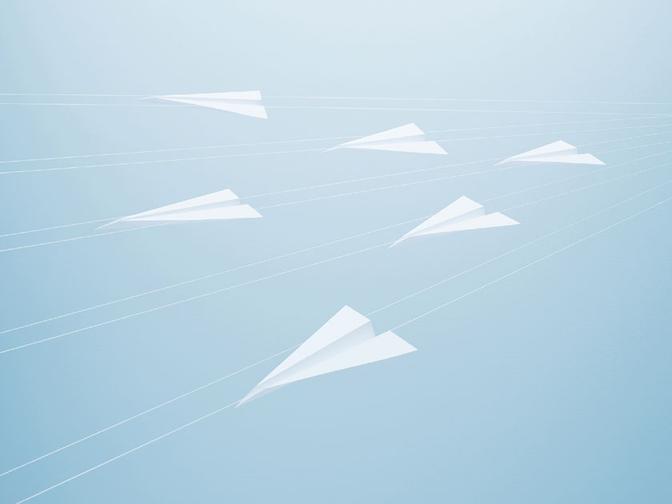 A collection of white paper airplanes in flight, suspended in mid-air against a blue background.