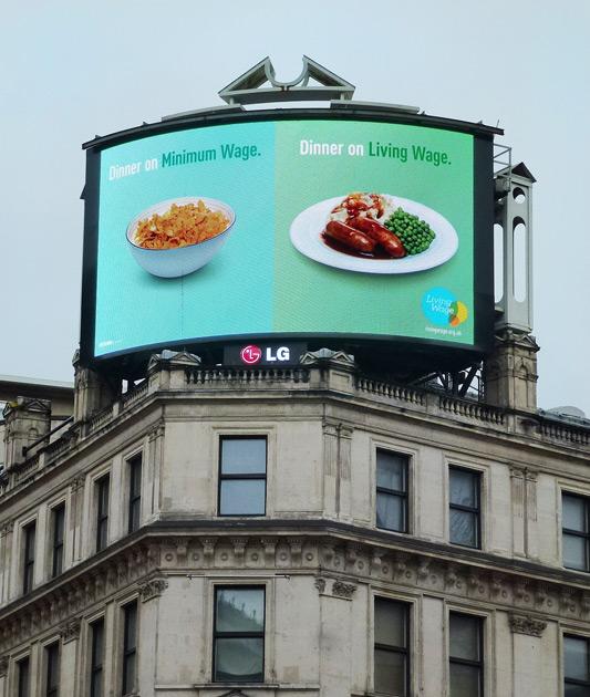Split-screen billboard showing bowls of food with 'Dinner on Minimum Wage' and 'Dinner on Living Wage' above each.