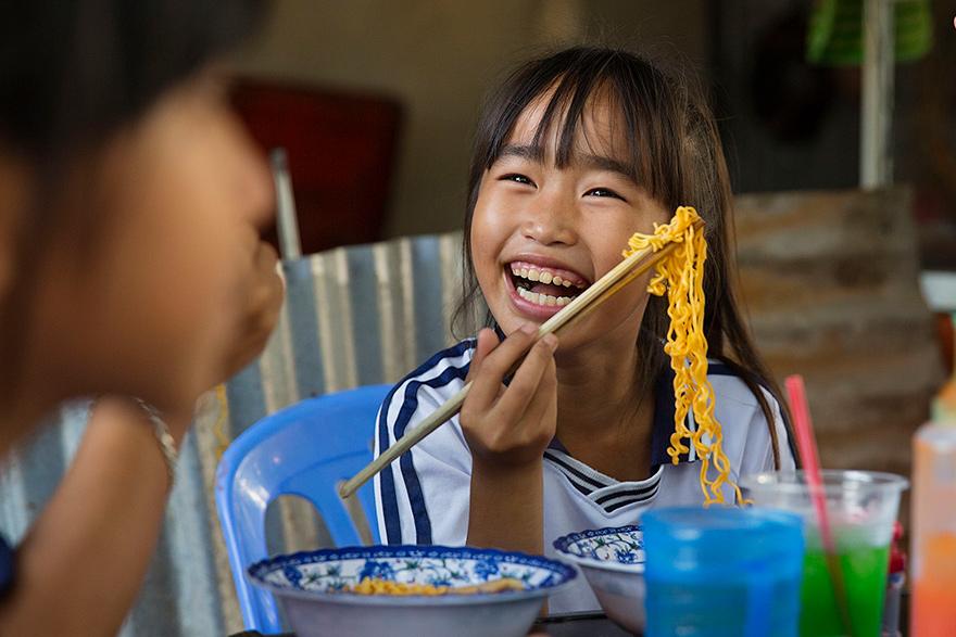A young girl eating noodles with chopsticks in a restaurant in Vietnam.