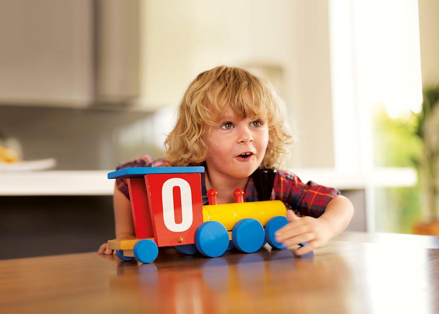 A young boy with blonde hair and a plaid shirt is playing with a toy train on a wooden table.