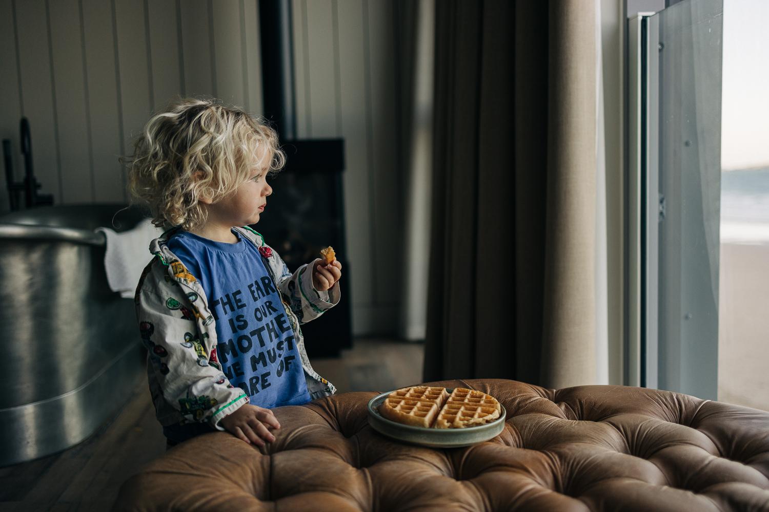 A child holds a waffle while looking out a window.