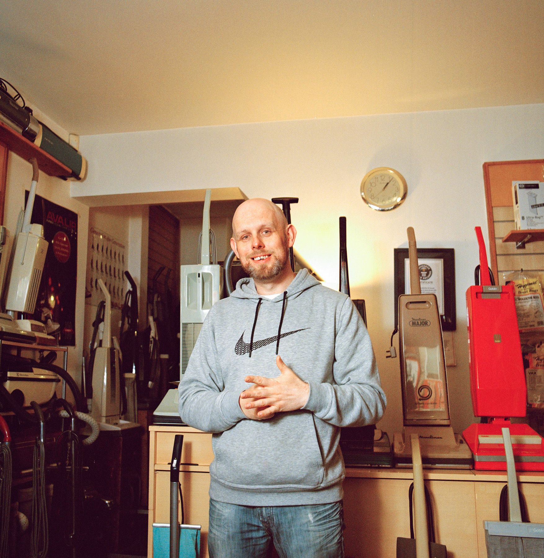 A man stands in a room surrounded by vacuum cleaners and cleaning equipment.