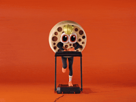 A person with a cartoonish, anthropomorphic pizza head is running on a treadmill, wearing a black and white striped running suit and white running shoes.
