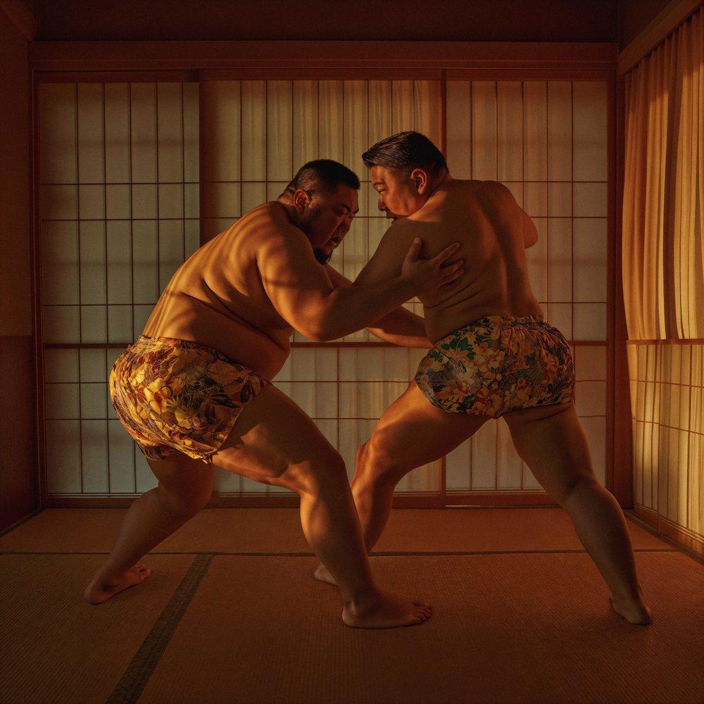 Two sumo wrestlers in traditional loincloths, or mawashi, facing off in a sumo wrestling match in a traditional Japanese sumo ring, or dohyo.