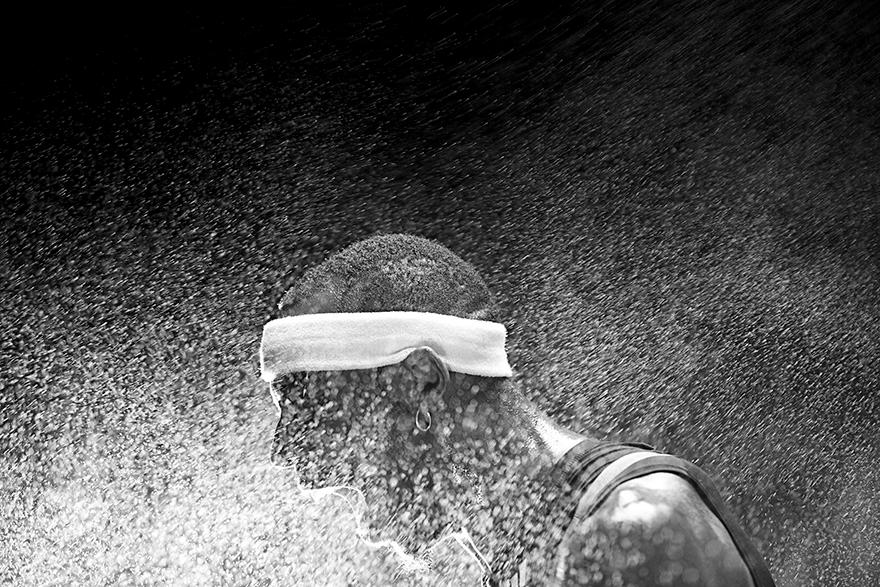A man in a sports jersey is running in the rain, with water splashing around him.