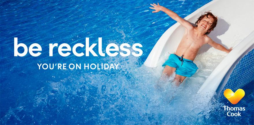 A young boy in a blue swimsuit is sliding down a water slide in a pool, laughing and having fun.