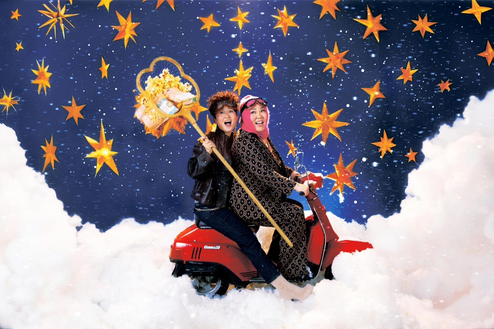 A man in a black leather jacket and jeans and a woman in a black and white patterned dress and pink scarf ride a red scooter through a snowy landscape under a starry night sky.
