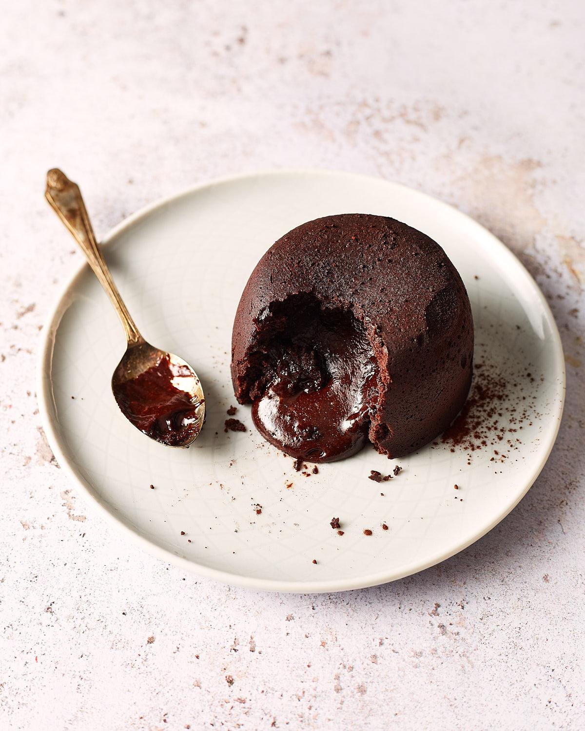 A rich, dark chocolate lava cake with a gooey, molten centre, served on a white plate with a gold spoon.