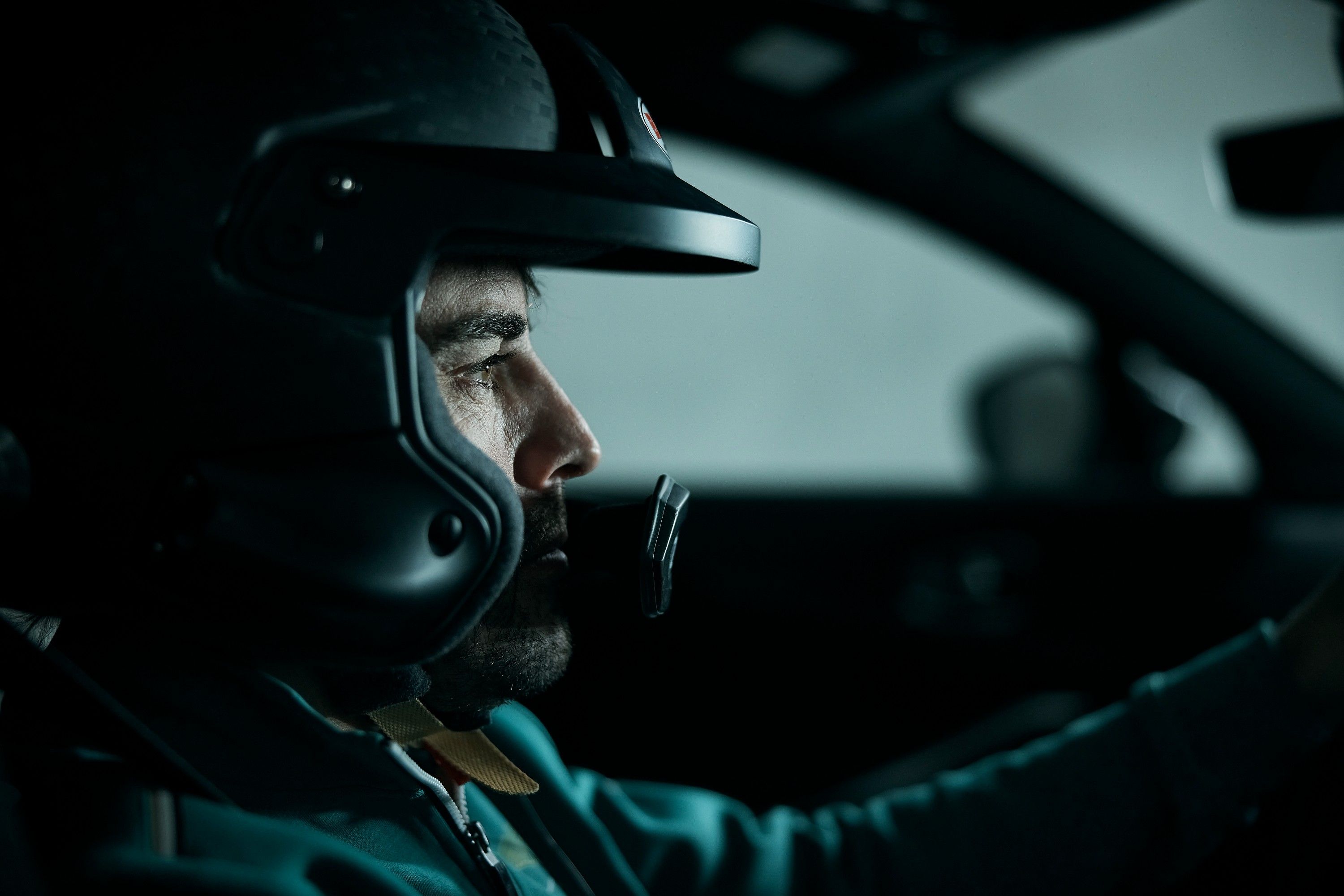 A close-up of a man wearing a racing helmet and a racing suit, with a focus on his face and the helmet's visor.