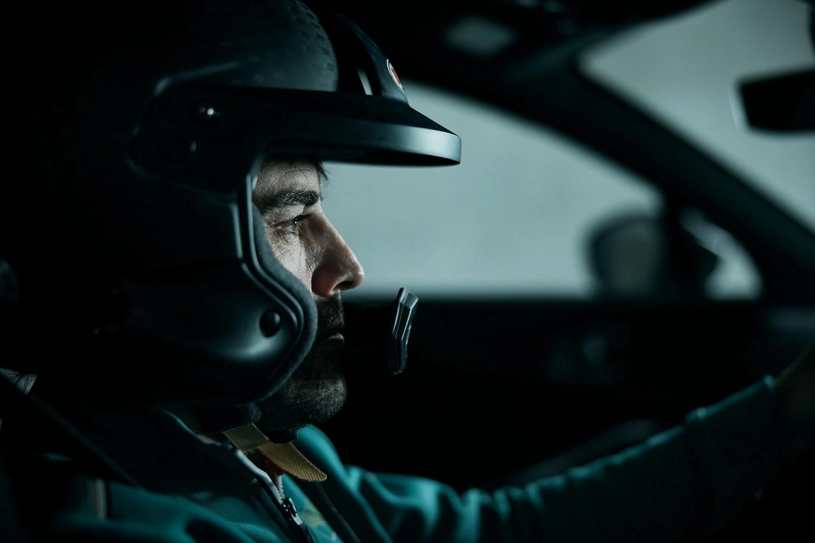 A close-up of a man wearing a racing helmet and a racing suit, with a focus on his face and the helmet's visor.