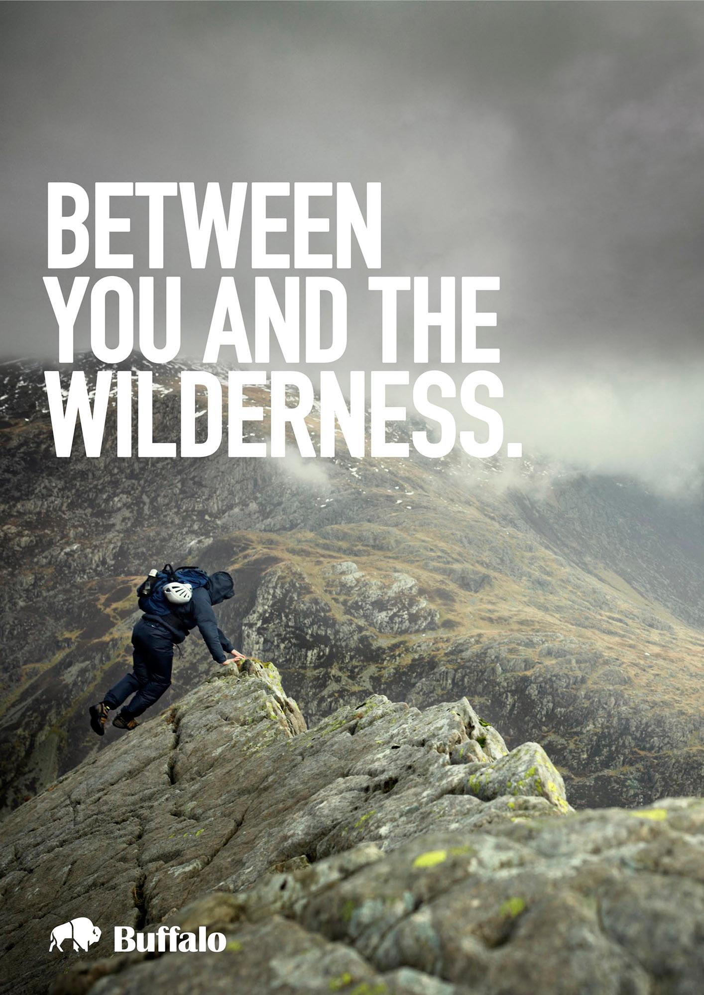 A person in a black jacket and pants is climbing a rocky outcrop in a mountainous landscape.
