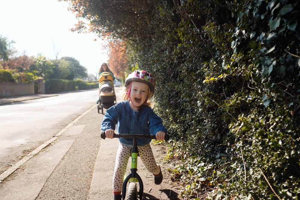 A young girl on a bike ride with her mother, both smiling and enjoying the sunny day. The girl is wearing a helmet and has a big smile on her face, while her mother is pushing a.