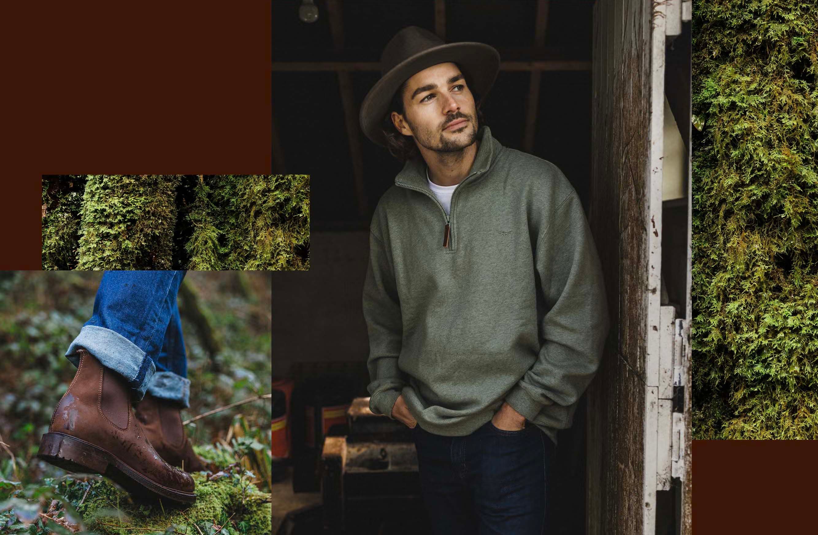 A man wearing a green quarter-zip sweater, jeans, and a hat, standing in a dark, moss-covered environment, with a focus on his clothing and surroundings.