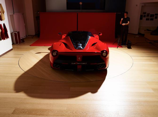 A red sports car is parked in a studio with a photographer and a backdrop.
