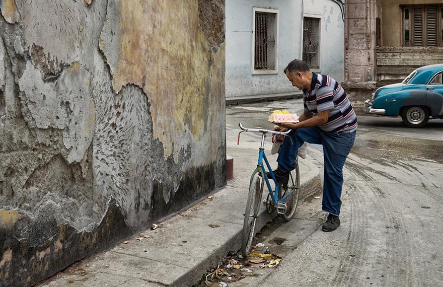 A man is sitting on a bicycle, eating a pastry from a street vendor.