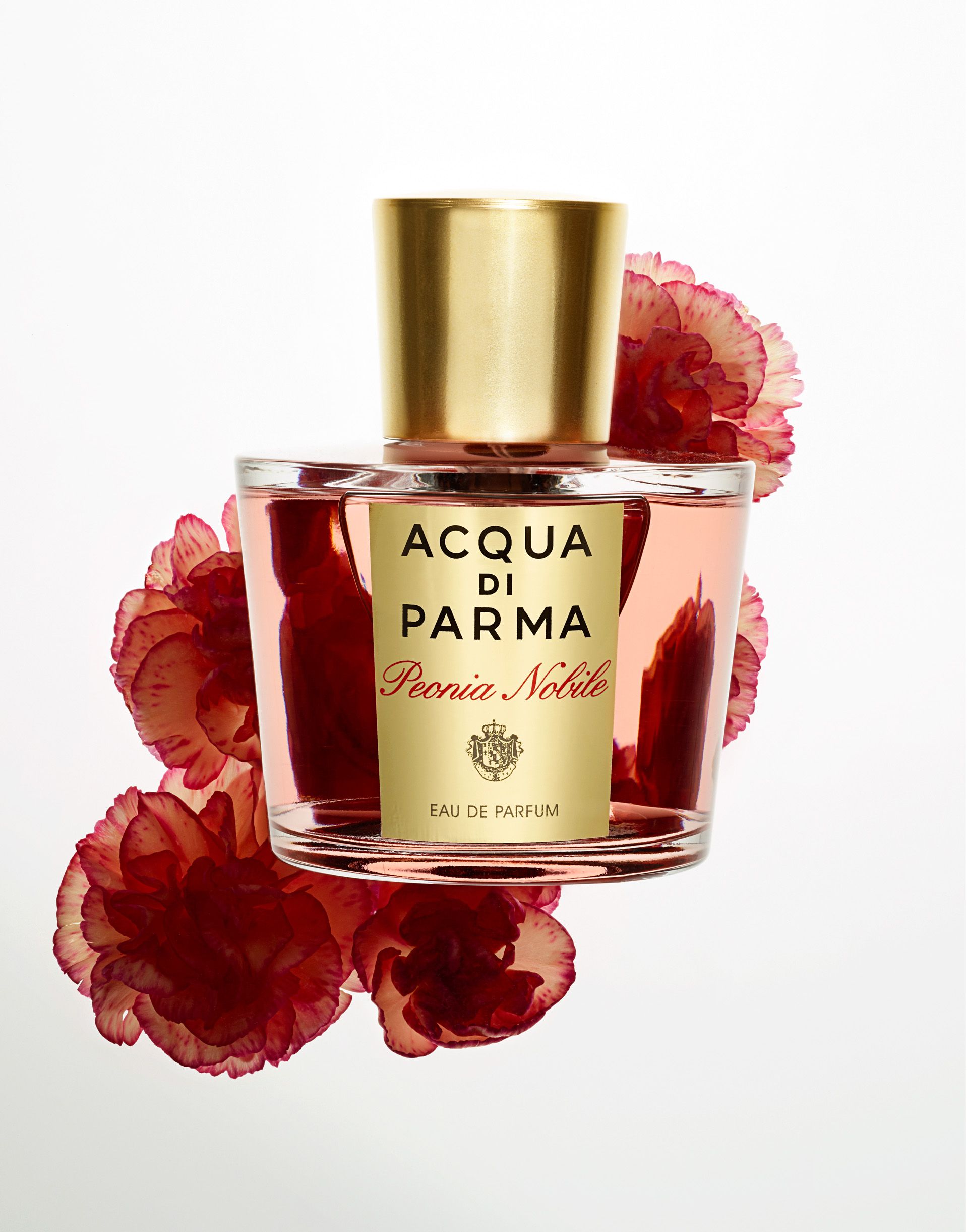 A glass bottle of perfume with a gold cap, surrounded by red flowers.