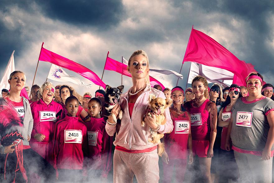 A group of people, including a woman in a pink tracksuit, holding a dog, surrounded by a crowd of people, some of whom are holding pink flags and wearing pink clothing.