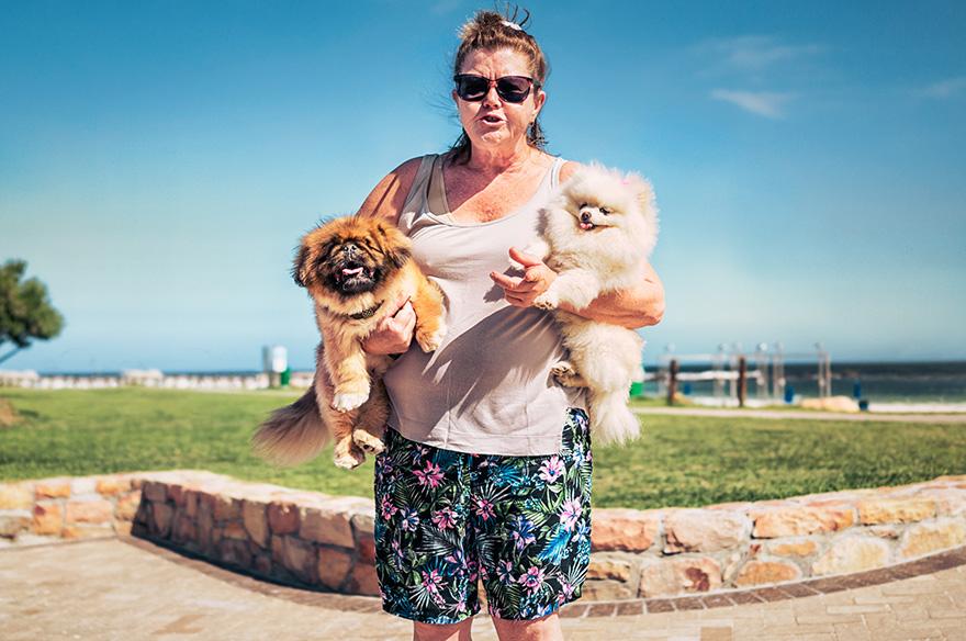 A woman holds two small dogs in a park.
