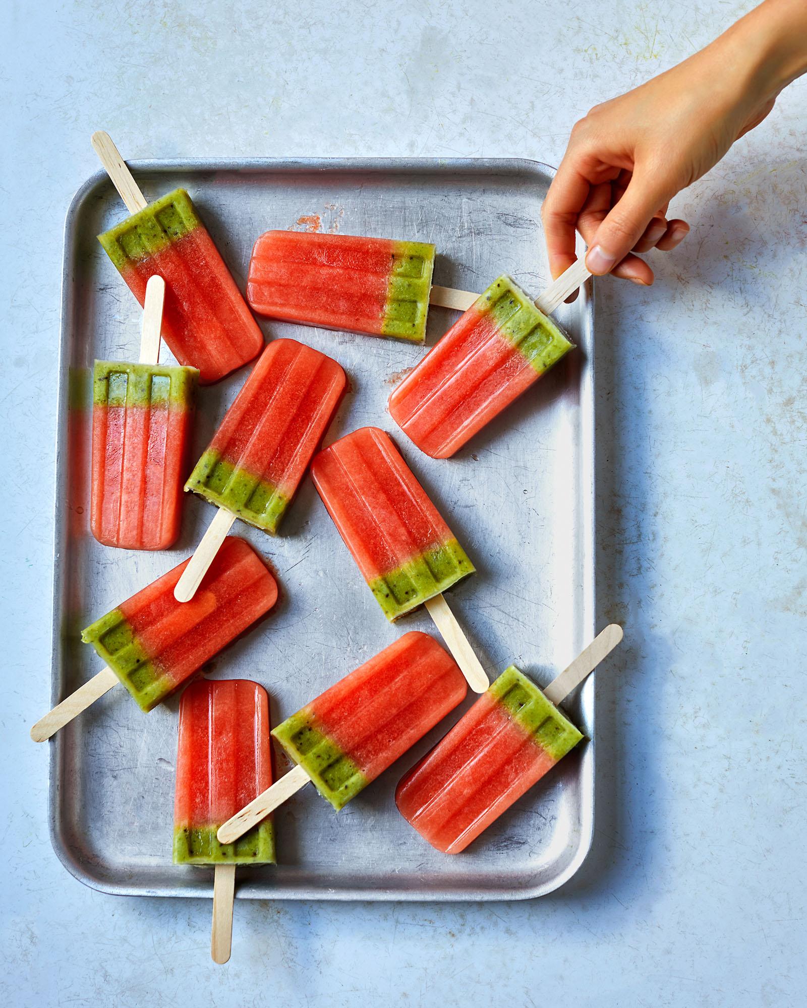 A tray of colorful, fruit-flavored popsicles, with a hand reaching for one.