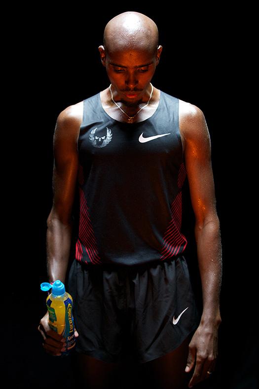 A man with a shaved head, wearing a black and red Nike running tank top and matching shorts, holding a sports drink bottle.