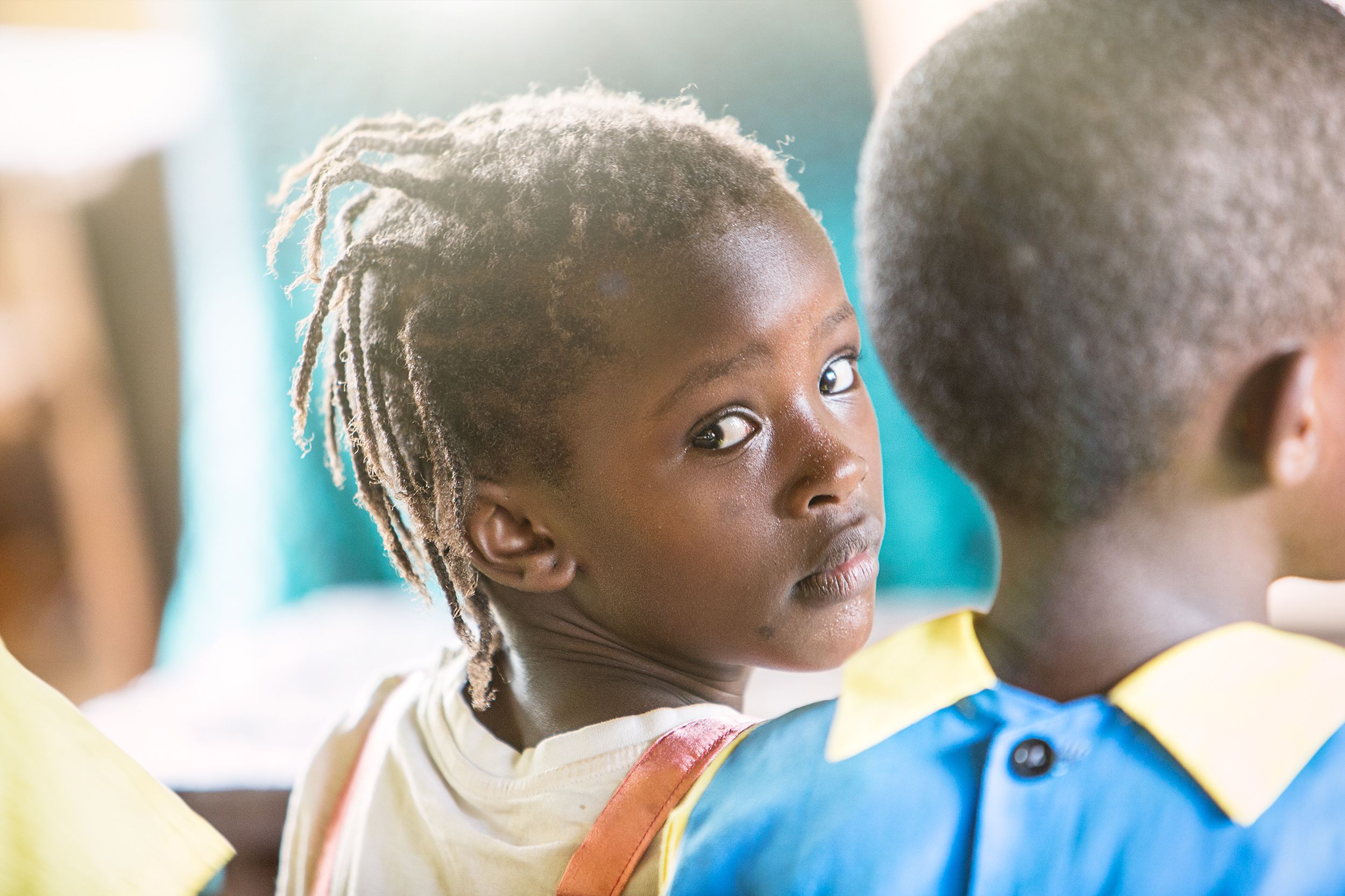 A young black girl with dreadlocks looks over her shoulder, smiling.