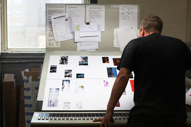 An image specialist for the artist is sitting at a desk with a large screen displaying a book layout, surrounded by papers and notes.