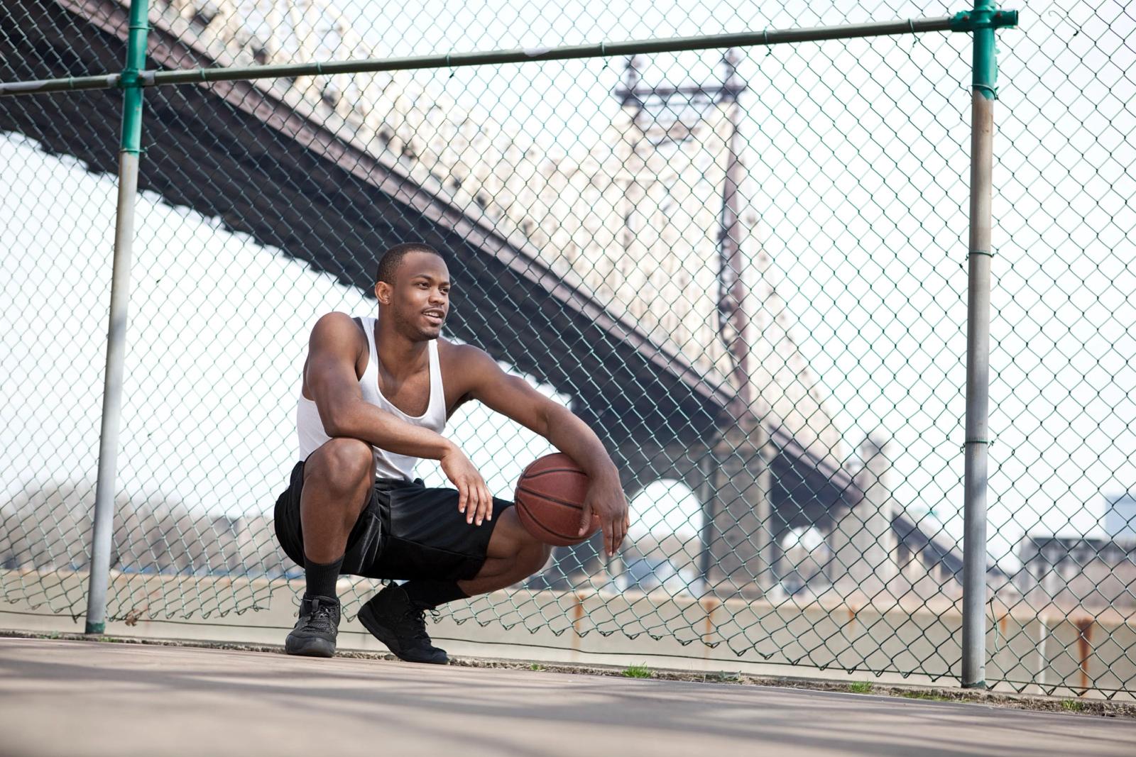 A man squatting on a basketball court holding a basketball.