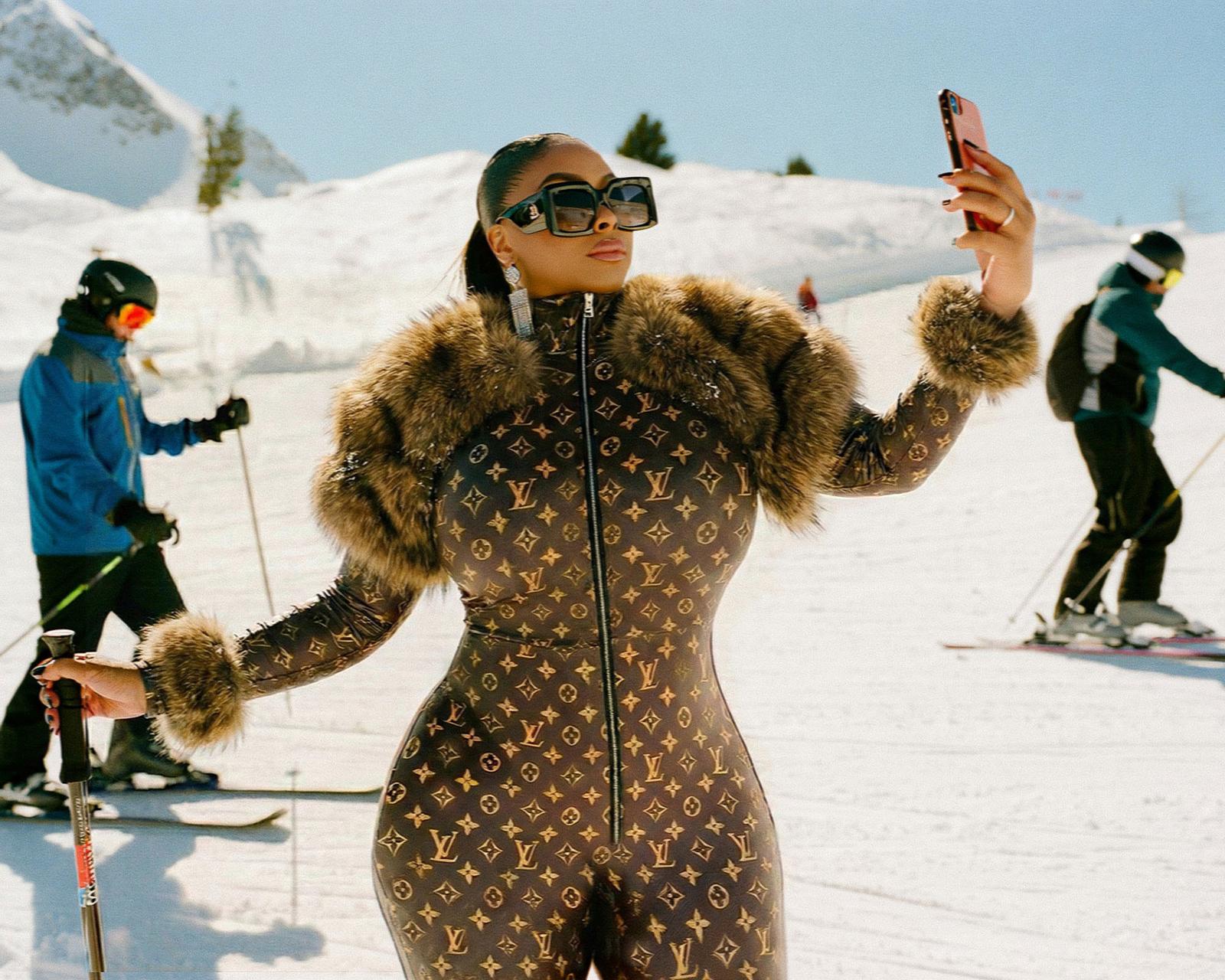 A woman taking a selfie on a snowy mountain while wearing a ski suit.