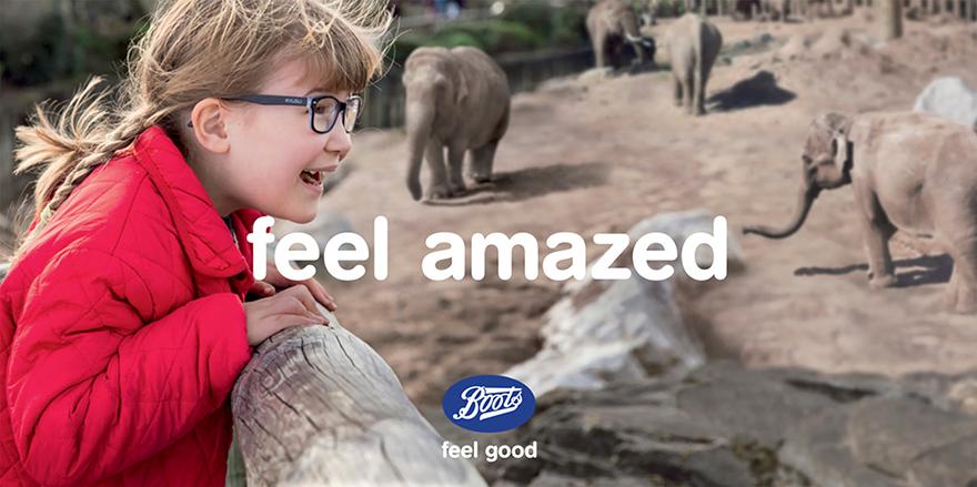 A young girl in a red coat looking at elephants in a zoo.