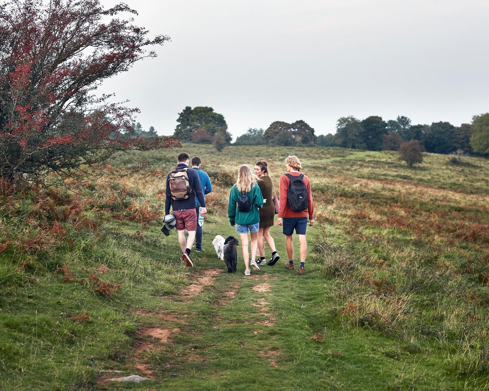 A group of people, including a woman with a dog, walking on a grassy hill in a rural landscape.