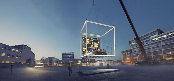 A large, empty, industrial-style building with a massive, white, metal, cube-like structure being lifted by a crane in the foreground, with a cityscape in the background.