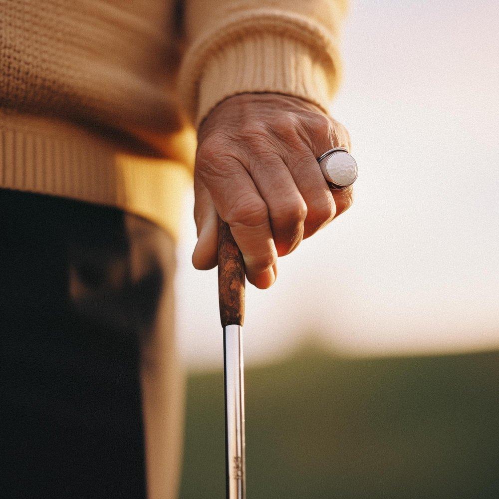 A close-up of a man's hand holding a golf club, with a golf ball on his finger, wearing a golfing glove and a golfing sweater.