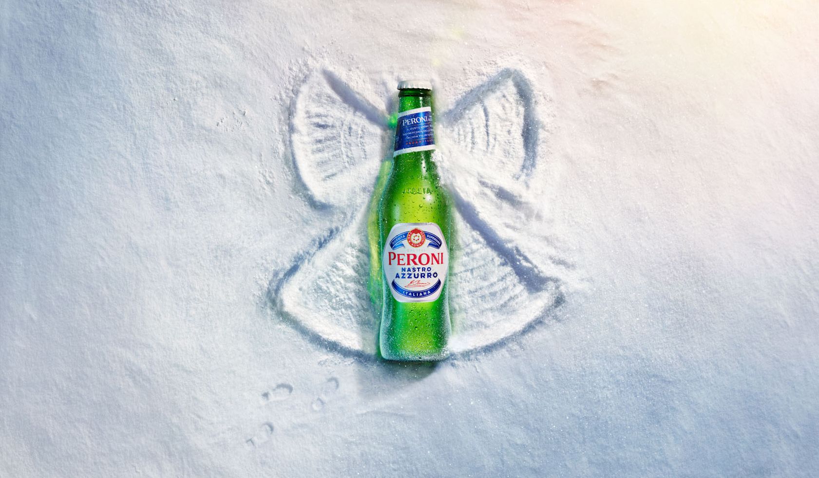 A green glass bottle of Peroni beer, partially buried in the sand, with a small, shallow, hand-drawn image of a fish in the sand next to it.