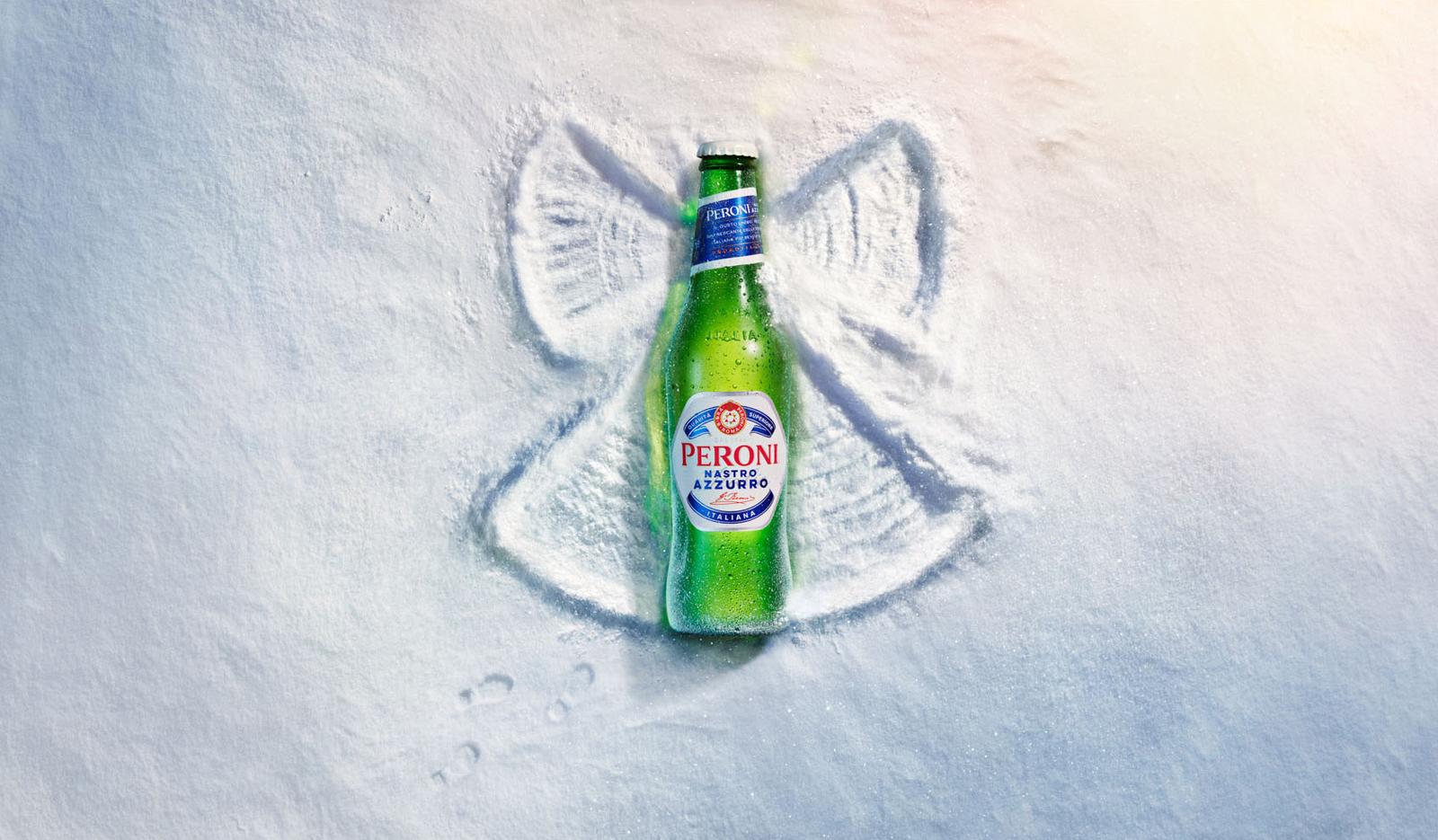 A green glass bottle of Peroni beer, partially buried in the sand, with a small, shallow, hand-drawn image of a fish in the sand next to it.