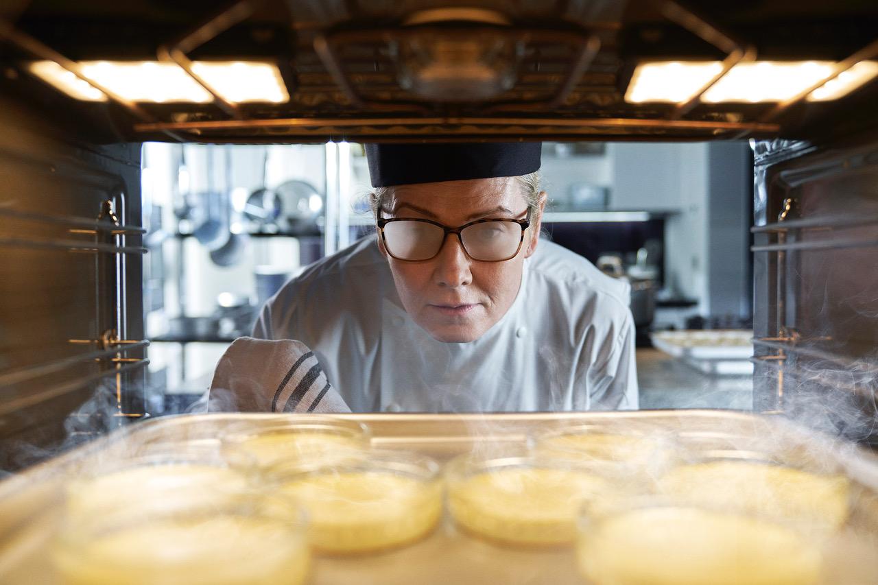 A chef looks into a hot oven containing golden-brown, round pastries.
