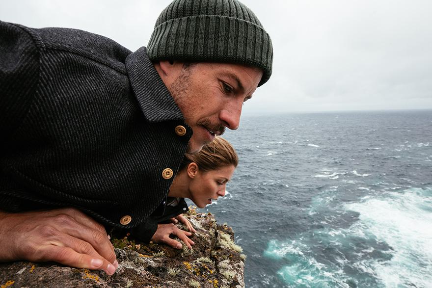 Two people, a man and a woman, are standing at the edge of a cliff, looking out at the ocean.