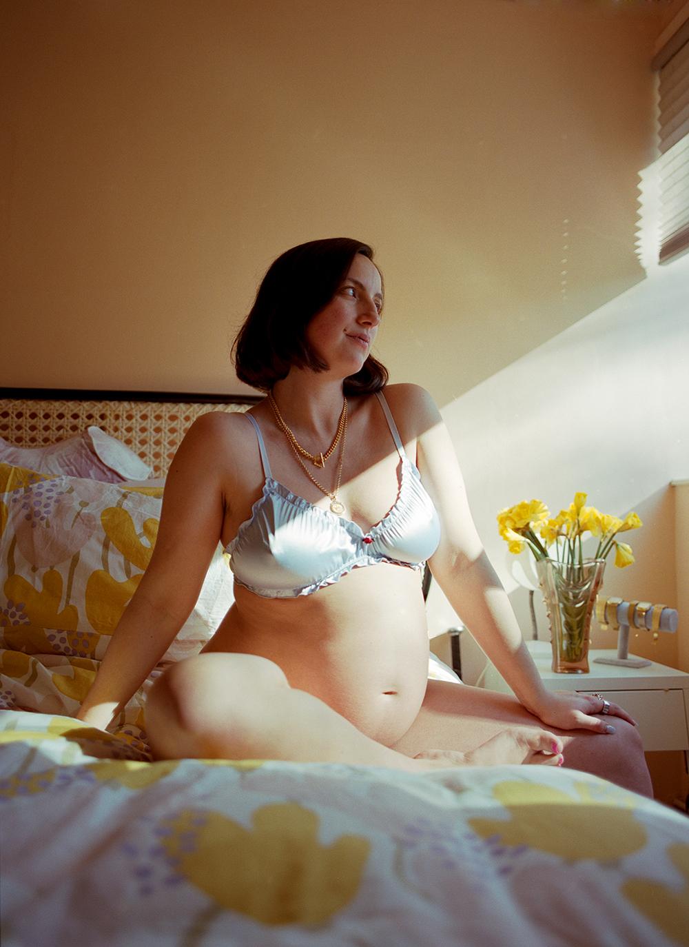 A woman in a white bra and underwear, sitting on a bed, looking directly at the camera with a mix of emotions on her face.