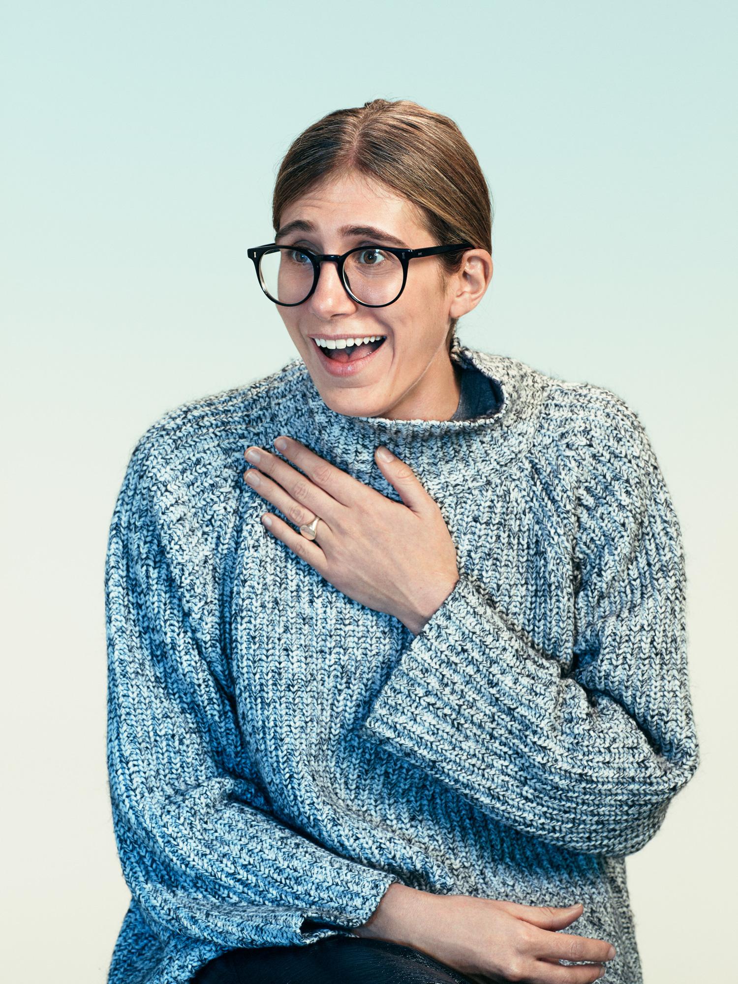 A woman with a surprised expression, wearing a blue and white sweater, with her hand on her chest.
