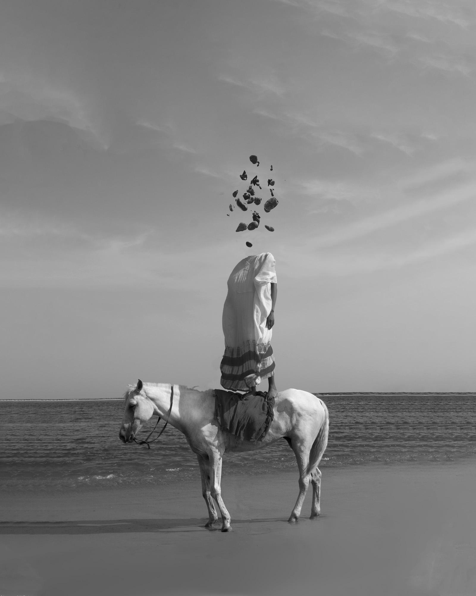 A person on a horse, wearing a traditional white robe, standing on a beach with the ocean in the background.