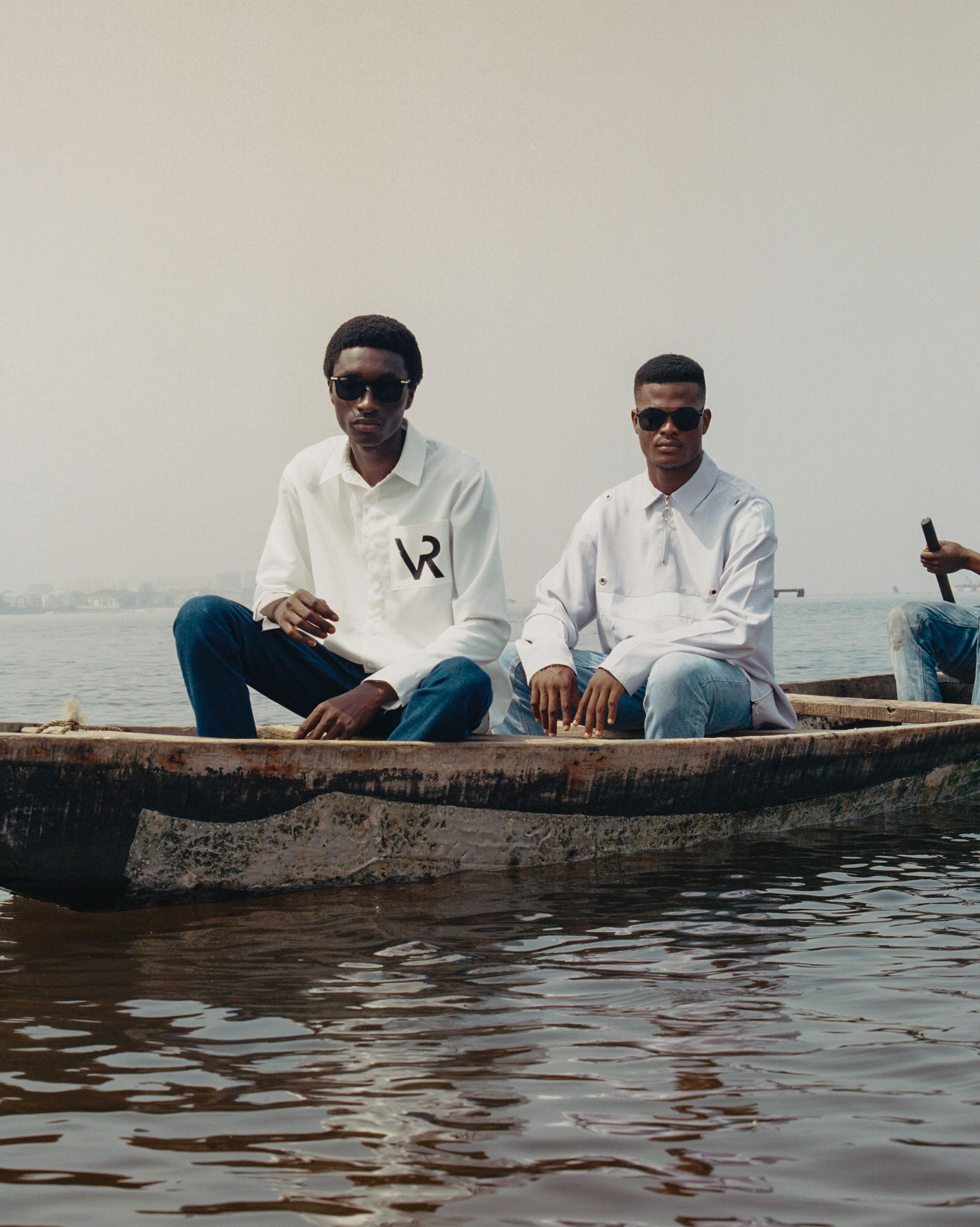 Two men in white shirts and jeans sitting in a wooden boat on a body of water.