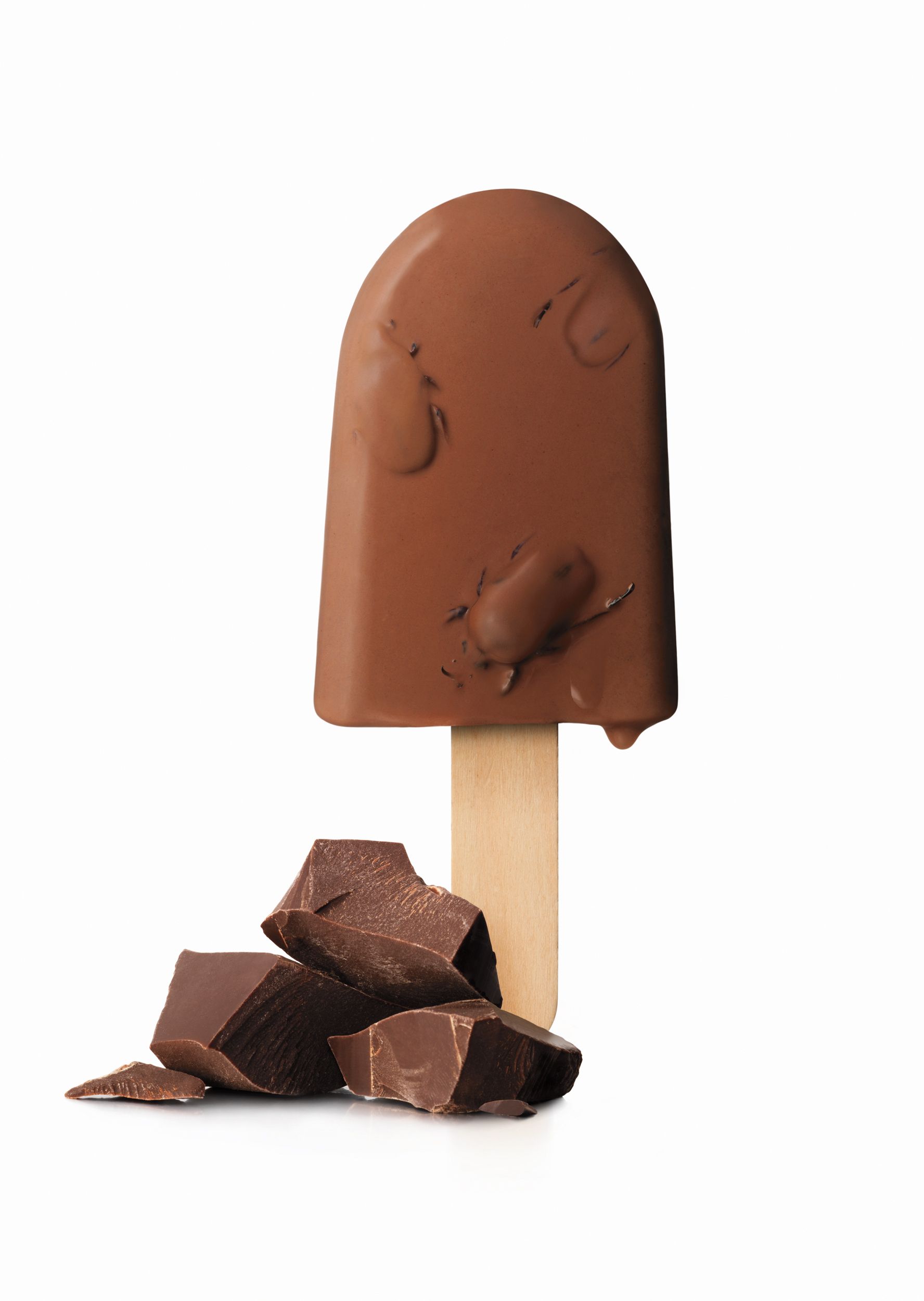 A chocolate ice cream on a stick, with a few pieces of chocolate broken off and scattered around the base.