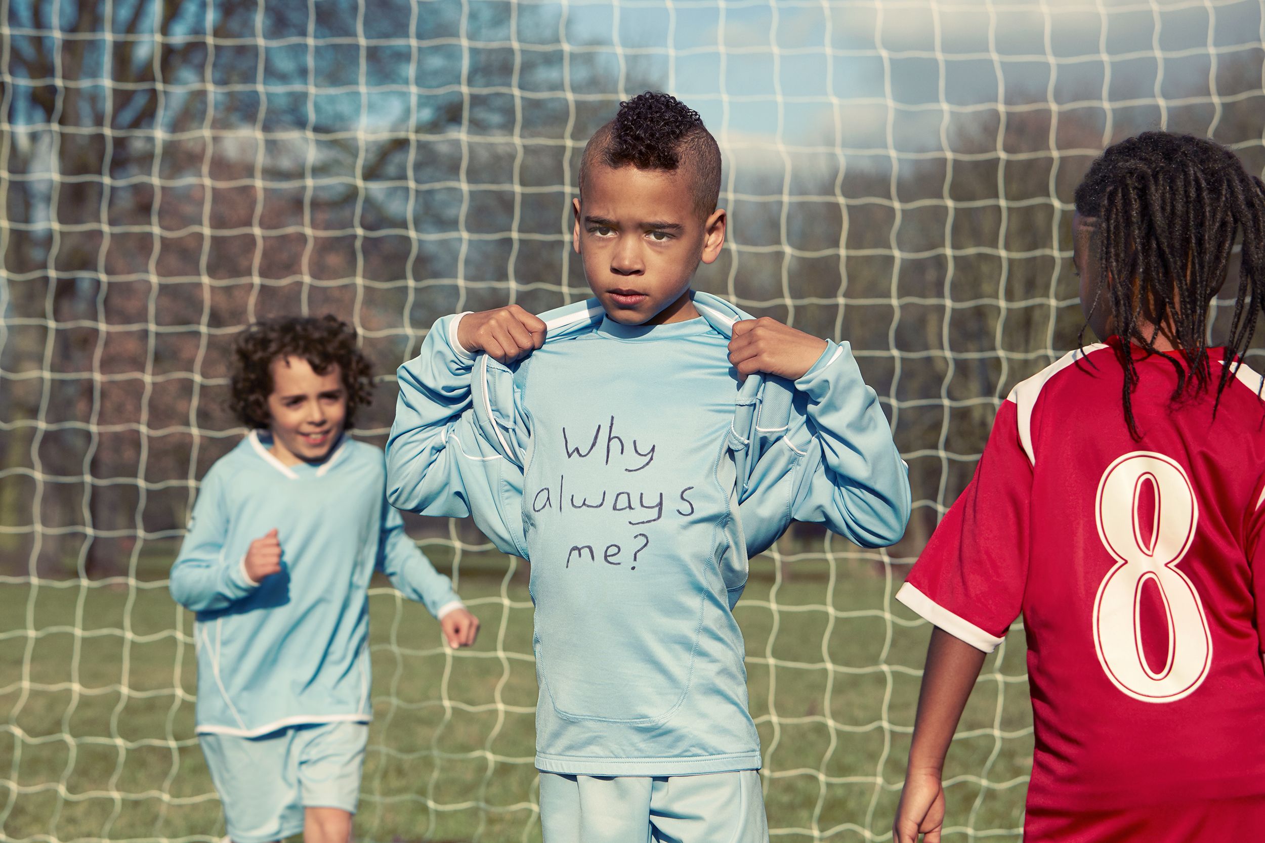 A group of children playing soccer, with one boy in a blue shirt saying 'Why always me?' and another in a blue jersey with number 8.