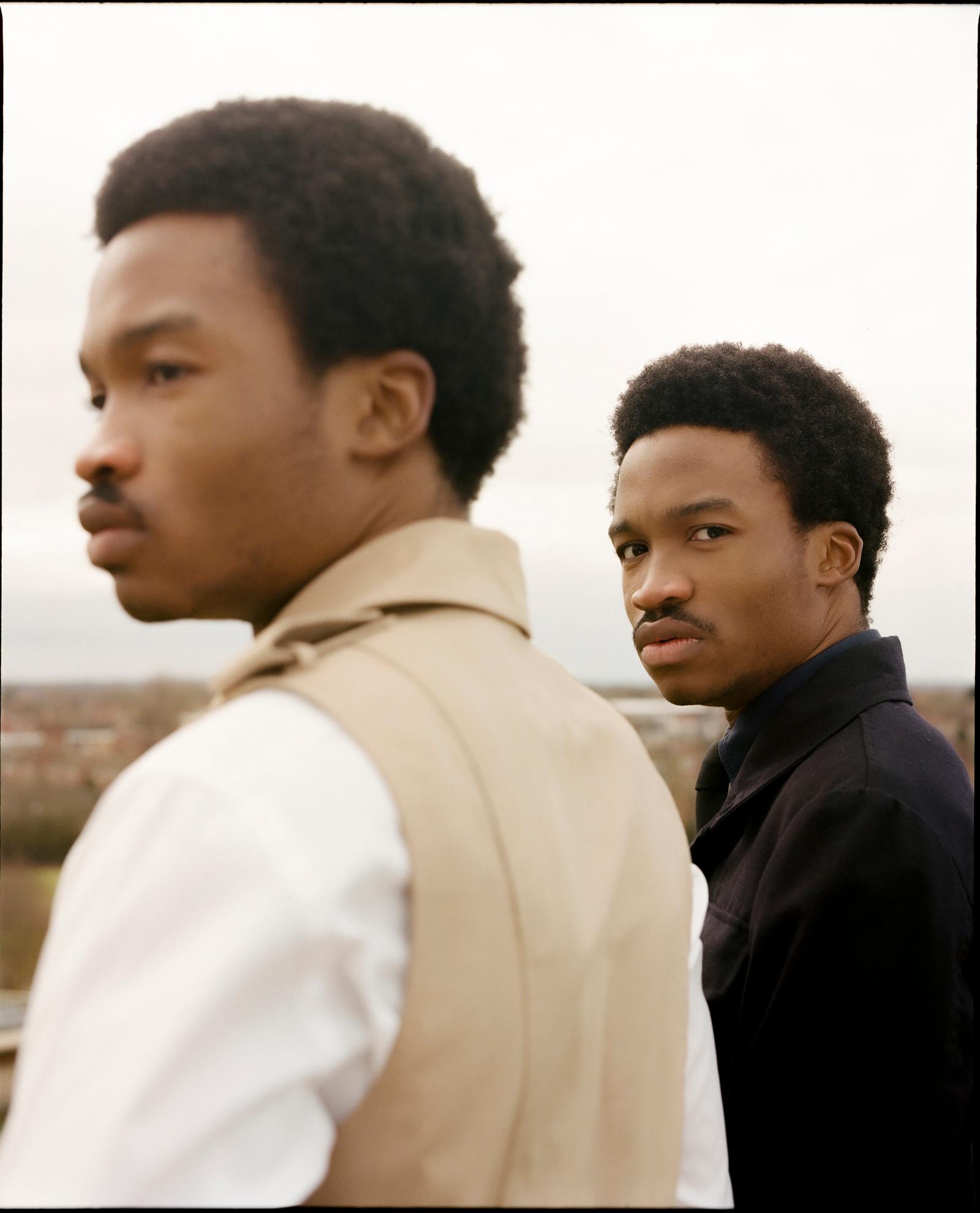 Two men stand back-to-back with faces turned to the side.